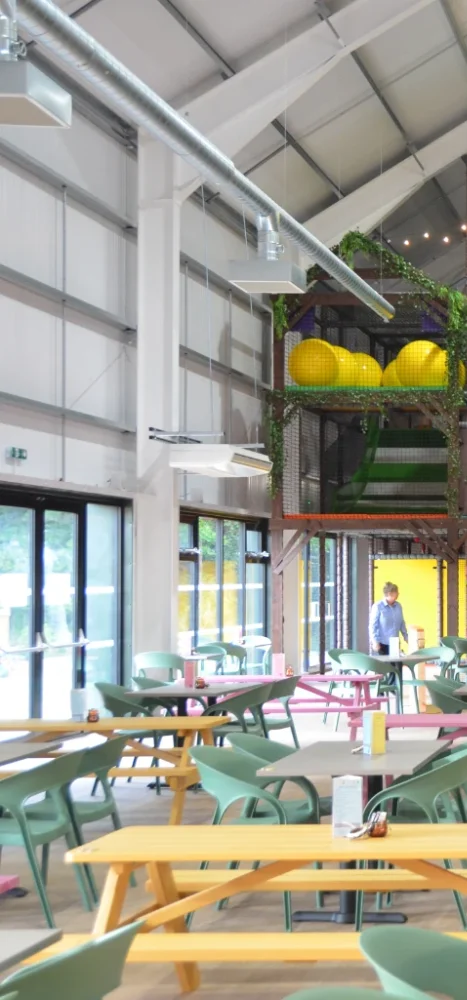 This is the first part of the main Brocksbushes feature image. This segment features the left side of the image. We can see yellow, pink and green table and chairs. A green and white slide and some yellow bounce yoga balls inside the softplay.