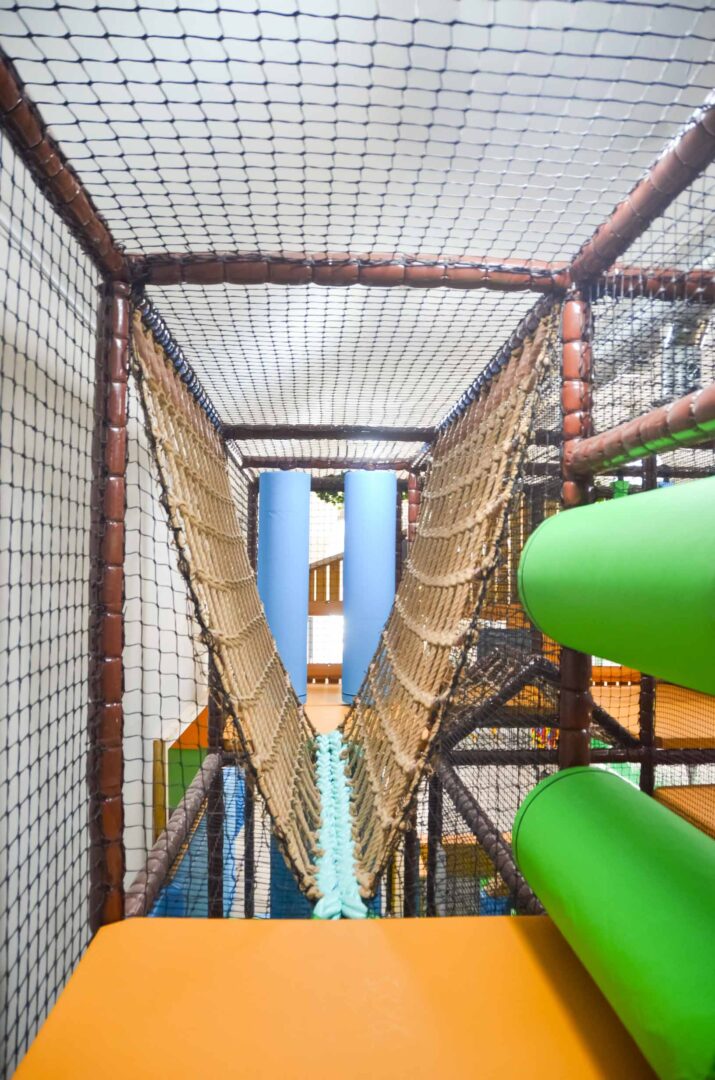 Blue and brown V-net rope bridge and green horizontal rollers at Thorpe Farm's indoor playground.