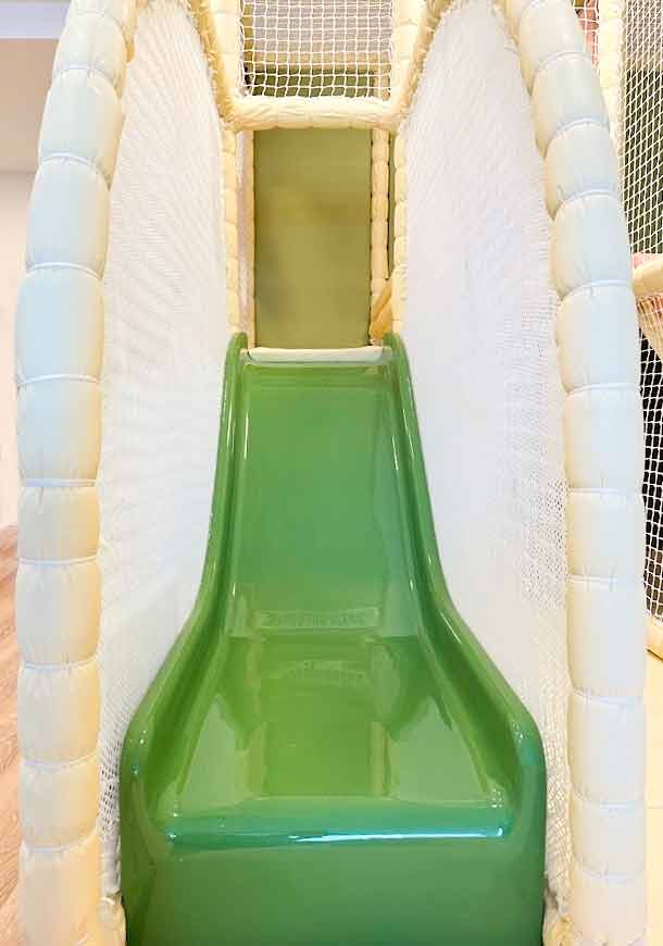 Green toddler slide with white rope net surrounding it. Found at Moo Moo's play cafe in Cobham.