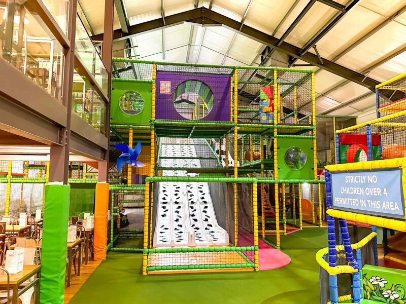 Cannon Hall Farm's multi-level indoor softplay. Featuring a green, yellow and purple colour scheme. There is a white and block cow print slide down the middle of it. The play area was designed by Play Creations