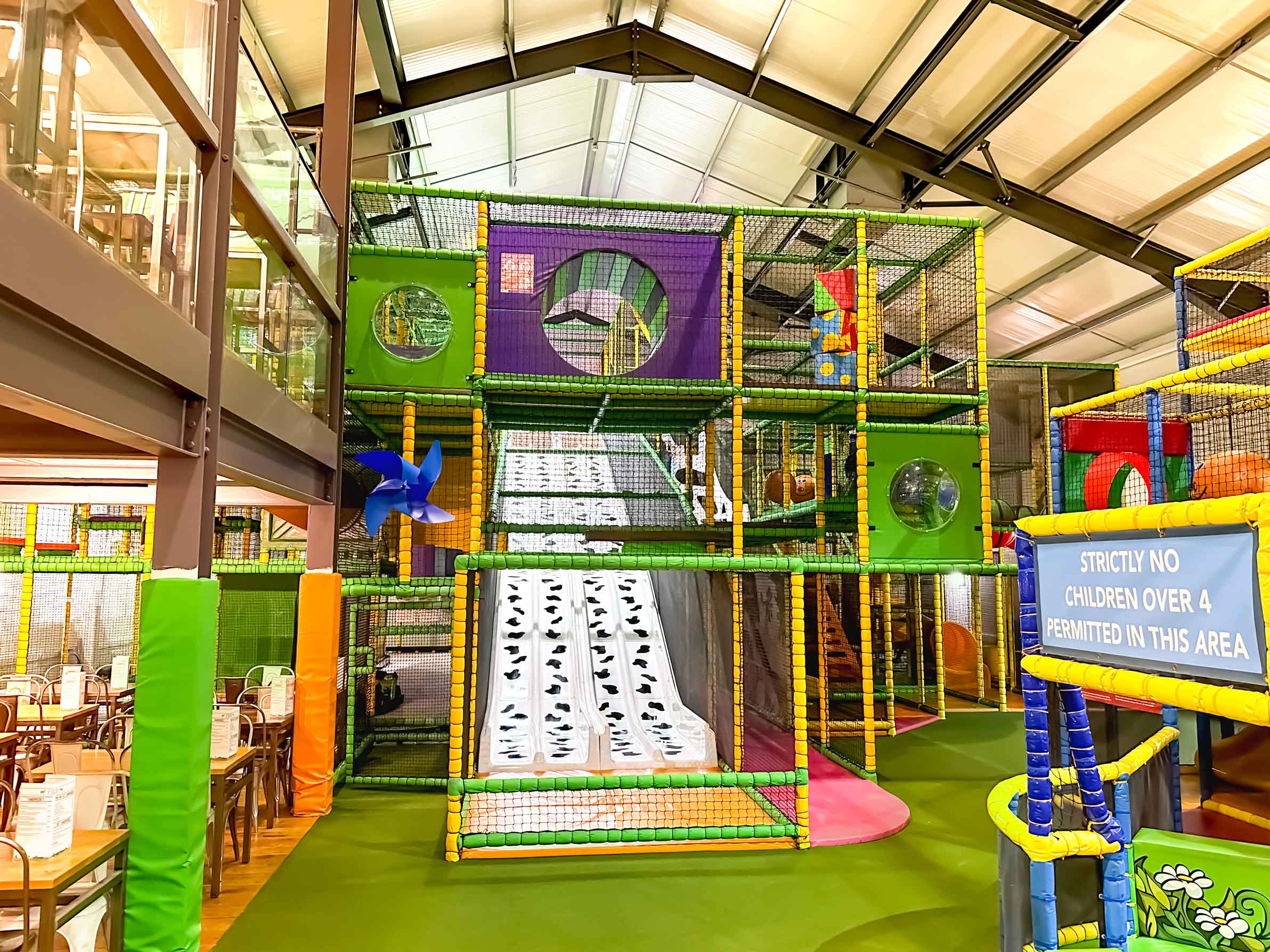 Cannon Hall Farm's multi-level indoor softplay. Featuring a green, yellow and purple colour scheme. There is a white and block cow print slide down the middle of it. The play area was designed by Play Creations