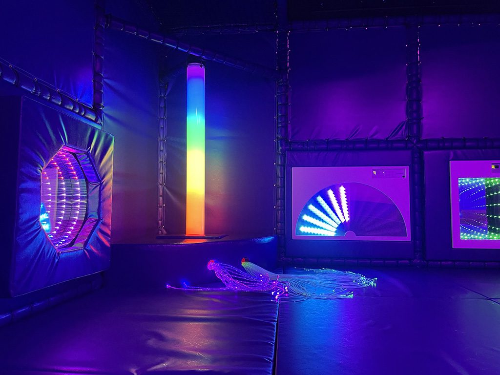 Wide view of all the sensory equipment at St Giles sensory area with a purple theme. The room features a LED light tube and 2 infinity mirrors.