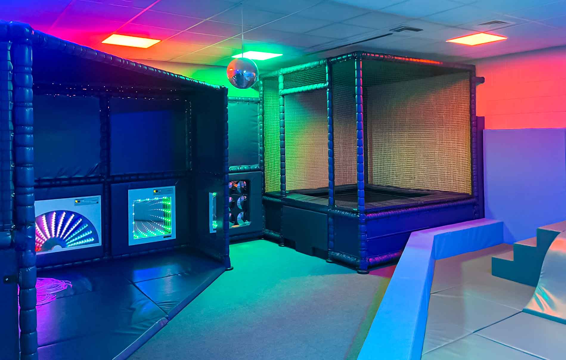 Wide shot of the whole sensory and movement room. Including the sensory nook, trampoline and movement area. Dark as the sensory lightsare on so colourful glow across the room.