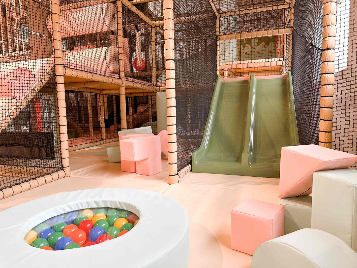 The Play Hut's indoor softplay dedicated baby area featuring a green twin toddler slide, some pink and white SOMA cubes and a white spinning ball pit. These were all designed by Play Creations