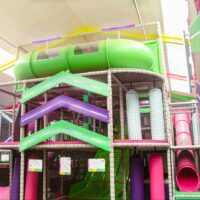 Fun Factory's multi-level green, pink and purple softplay structure that features a green wavy slide, green crawl tube, vertical rollers and bright LED arrows on the front.