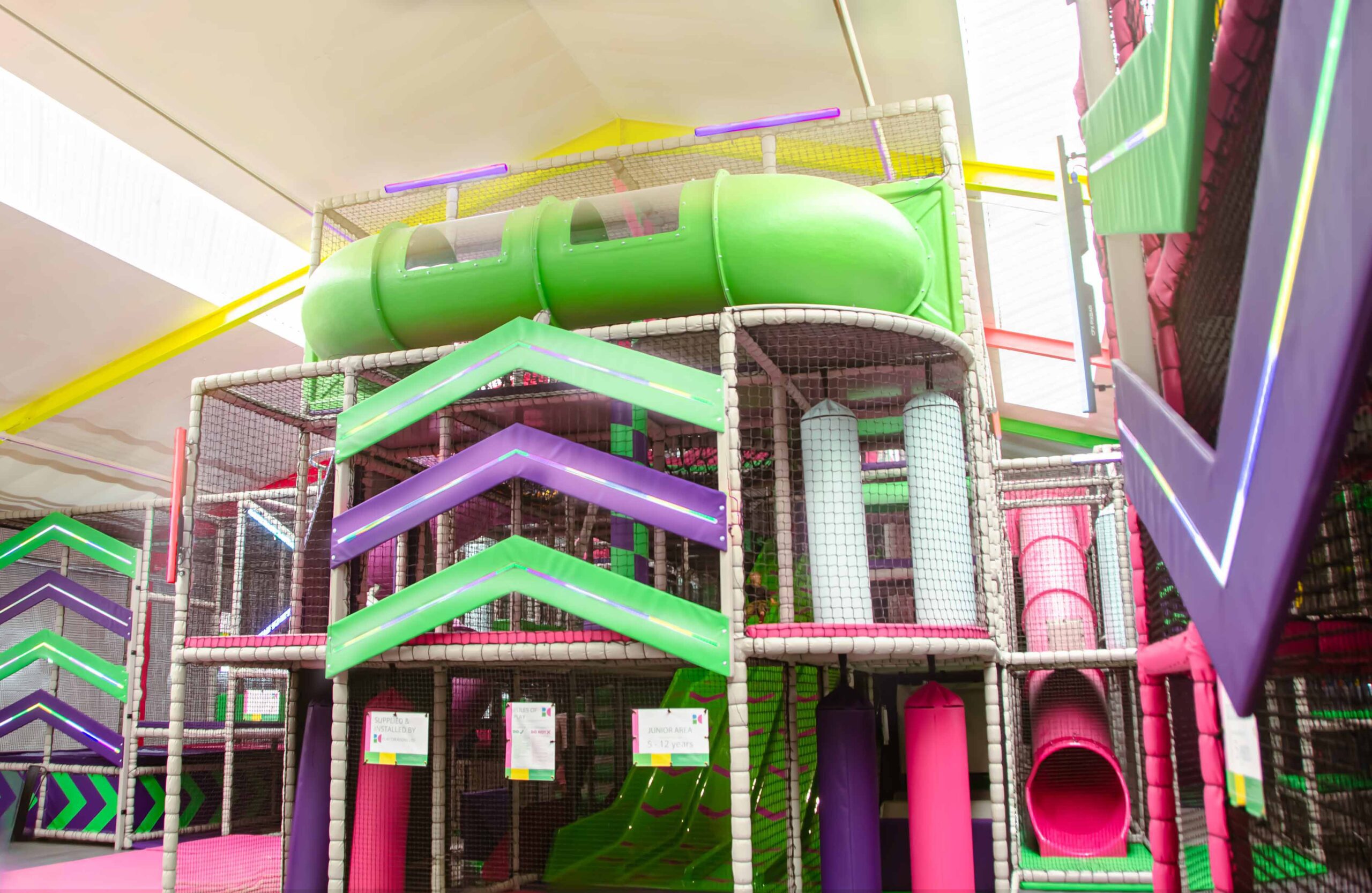 Fun Factory's multi-level green, pink and purple softplay structure that features a green wavy slide, green crawl tube, vertical rollers and bright LED arrows on the front.
