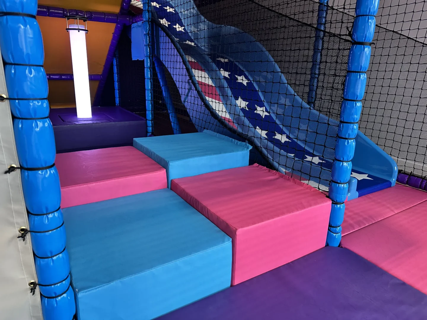Pink and blue wedge floor, LED Light tube in purple plinth and a stars and stripes themed twin astra slide. These are all found at RAF Lakenheath's indoor softplay area designed by Play Creations.