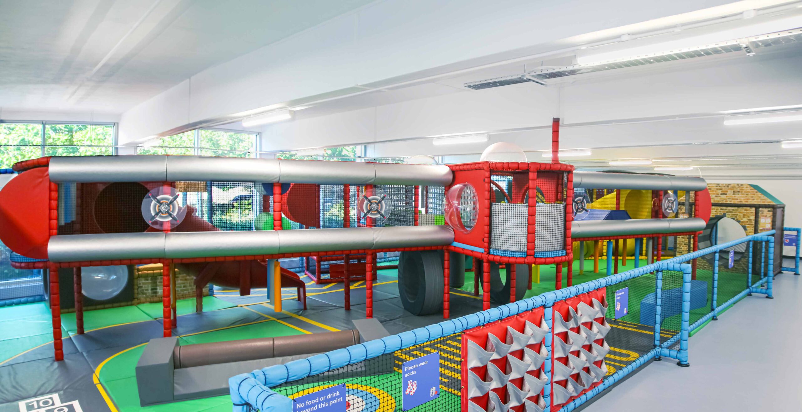 RAF Museum's indoor softplay featuring an aviation theme. The softplay is designed to look like a plane with a red and silver theme. The ground represents a runway to match the theme. Designed by Play Creations.
