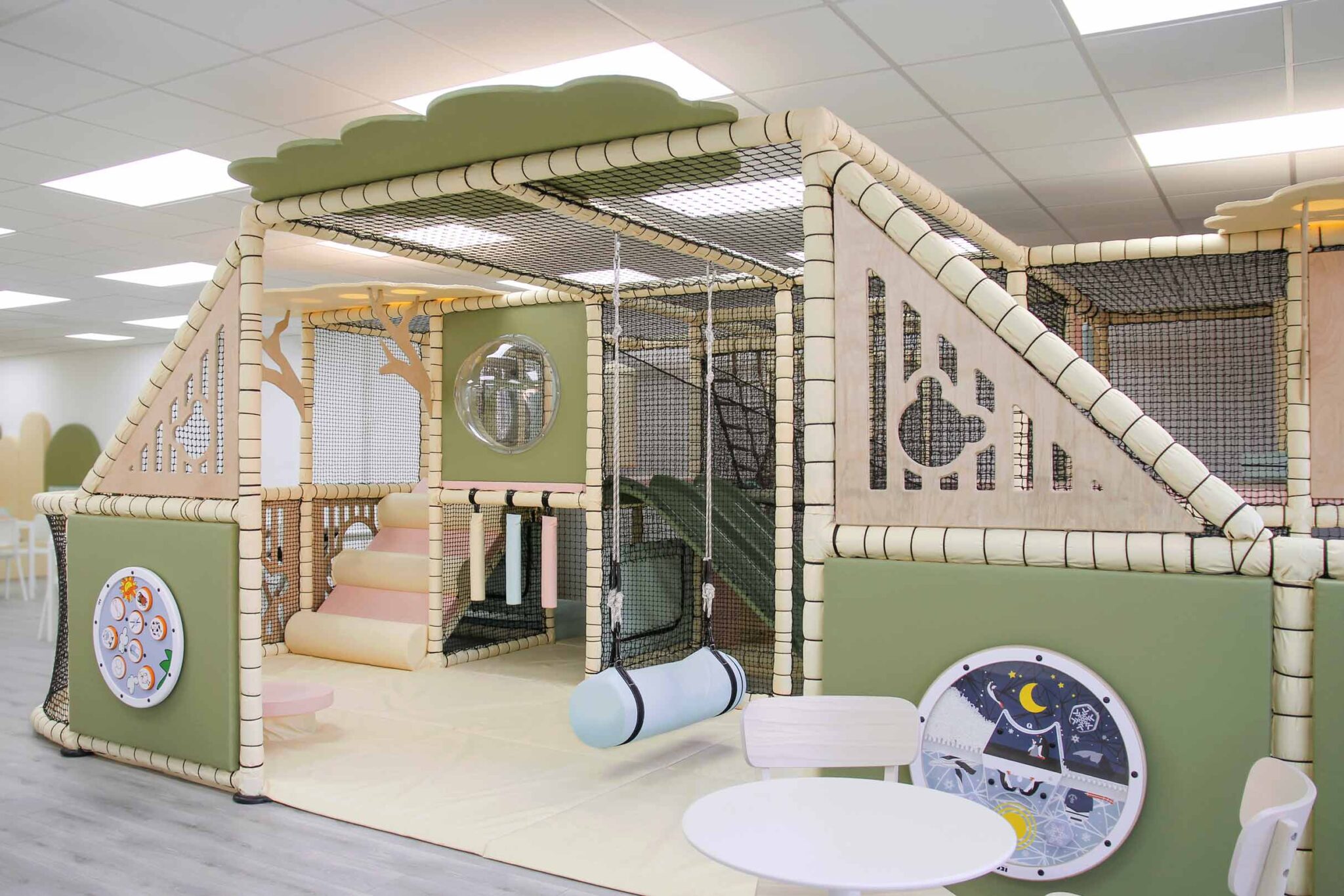 Cub and Cup Softplay Cafe in Swindon. The color scheme is cream, green, pink and blue which complement the cozy atmosphere. There are bear wooden features that are on the side of the softplay. Alongside bespoke tree panels to add to the aesthetics.