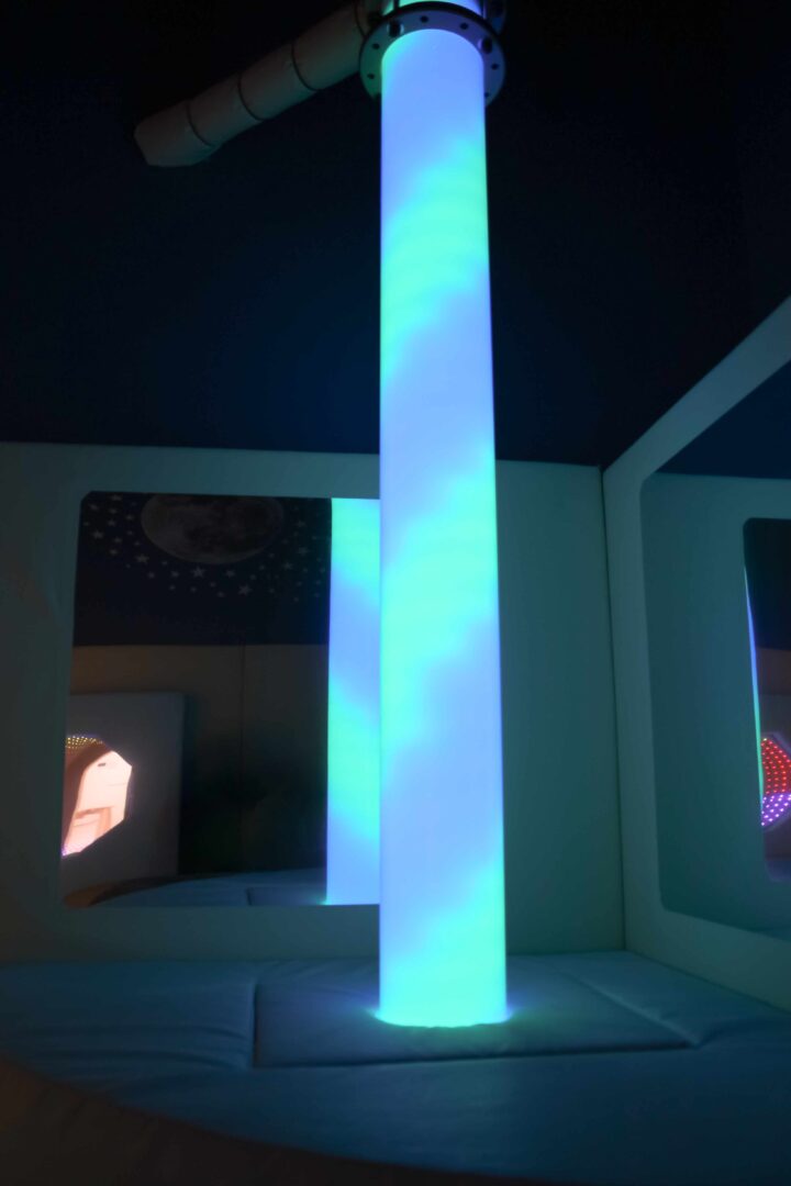 Colour-changing LED Light Tube at Cub and Cup's play cafe. The lamp is in a dark sensory room and is lit up blue and purple.